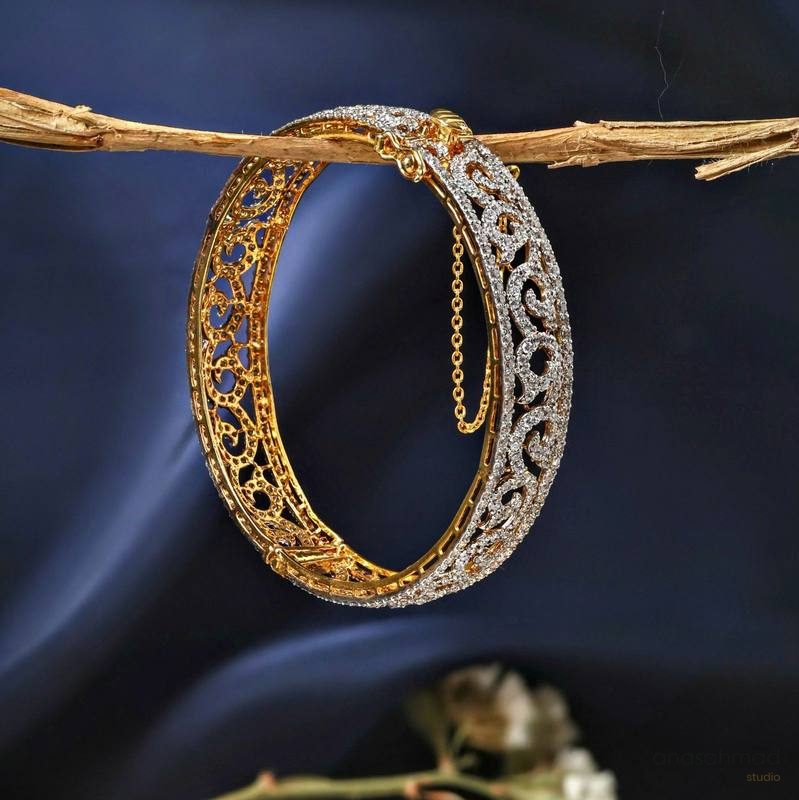 Gold and diamond filigree bangle suspended from a branch against deep blue silk