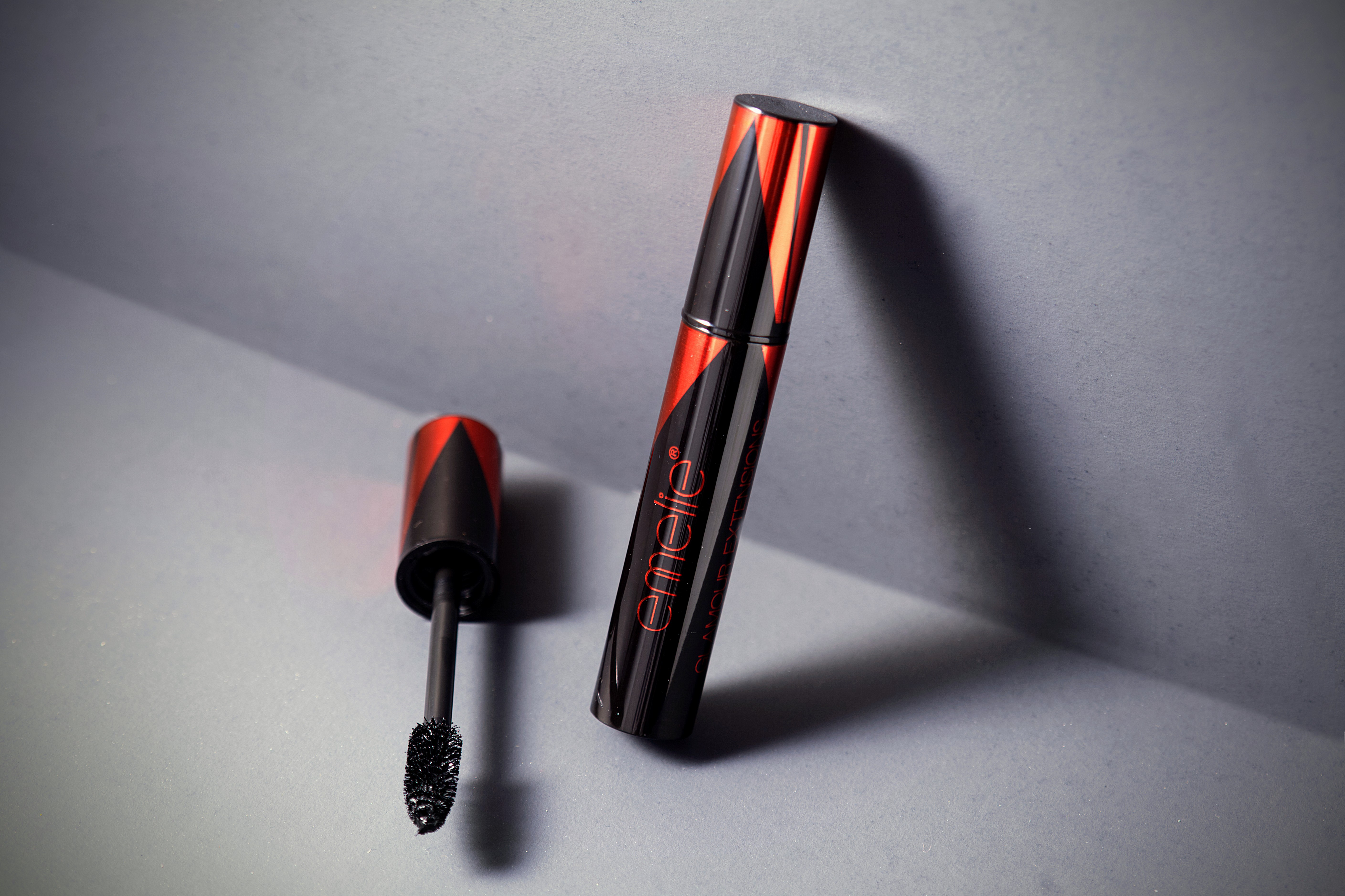 Black mascara tube with applicator wand on grey background