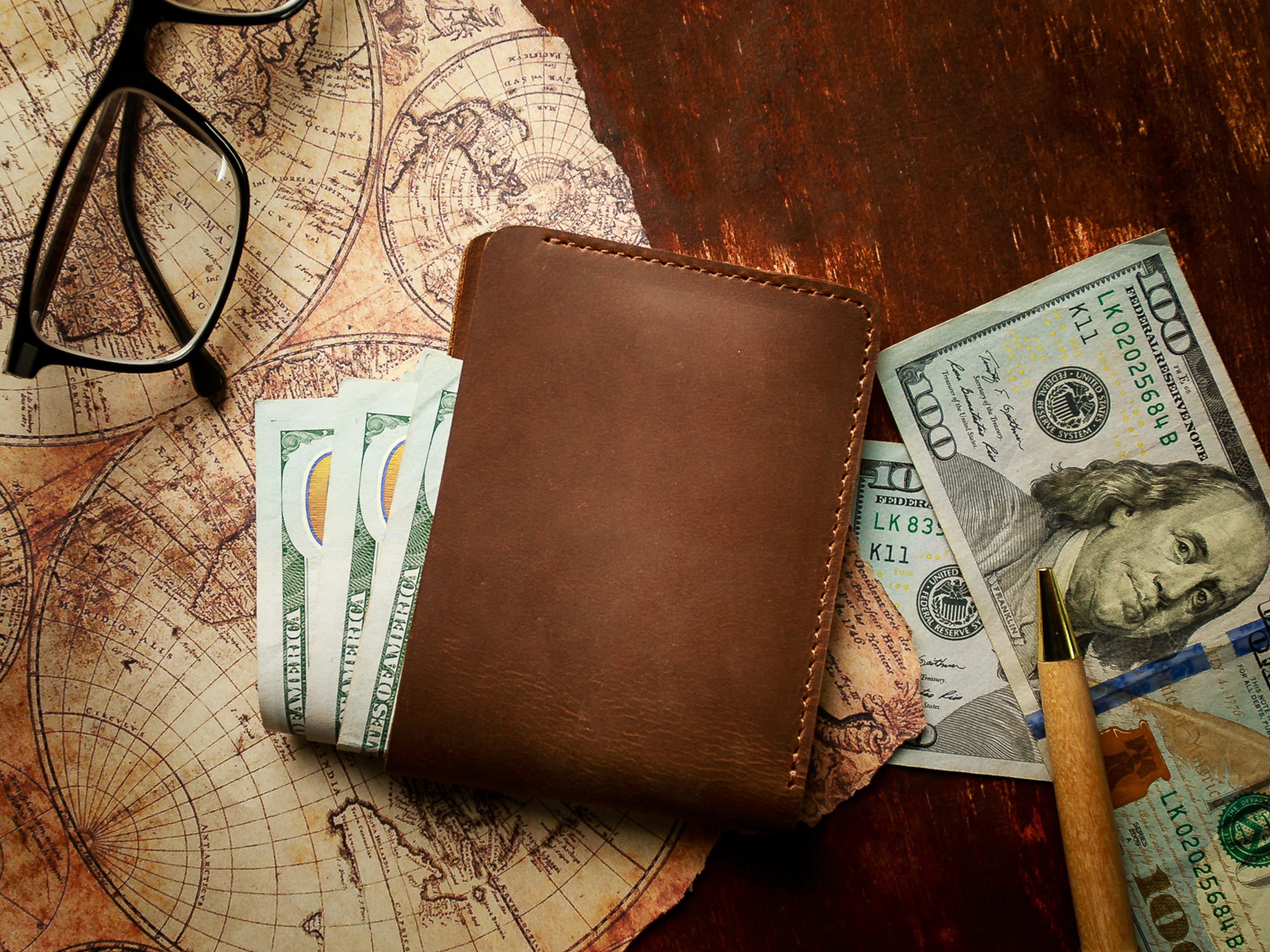 Brown leather wallet with US dollar bills on vintage map background