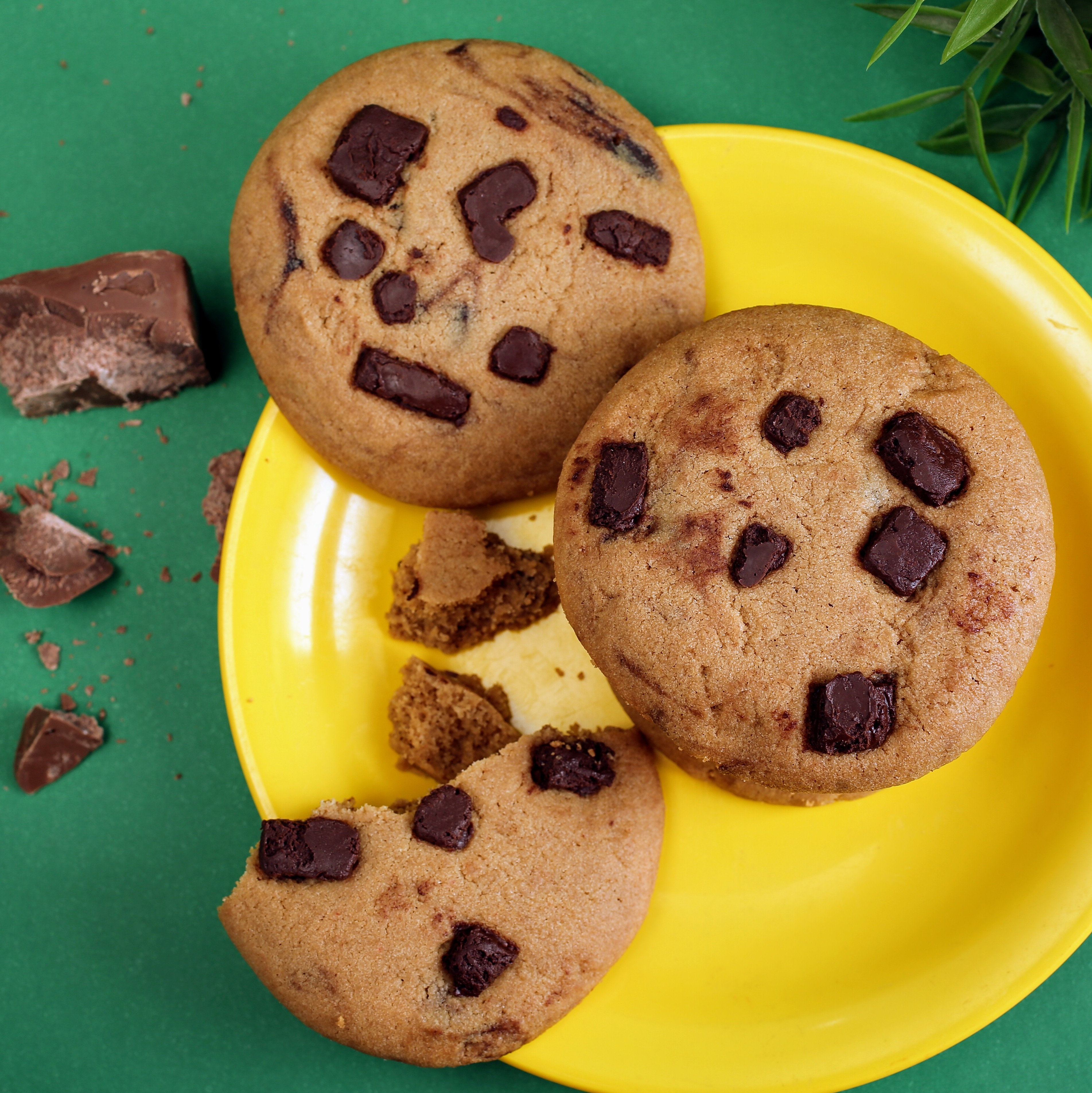 Homemade chocolate chip cookies on a yellow plate with chunks of chocolate