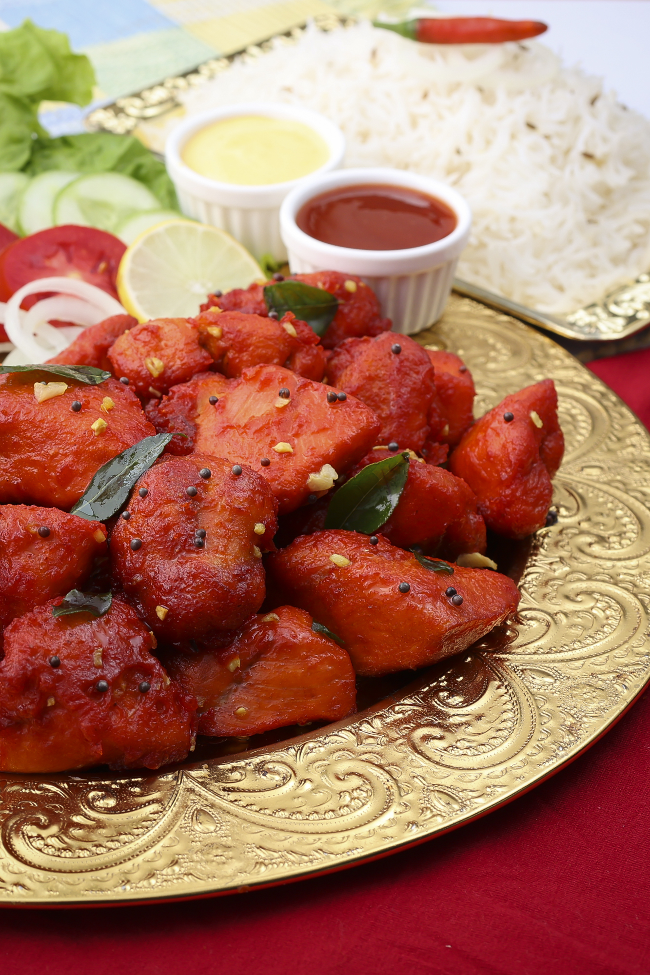 Spicy chicken tikka pieces served on a decorative plate with chutney and rice