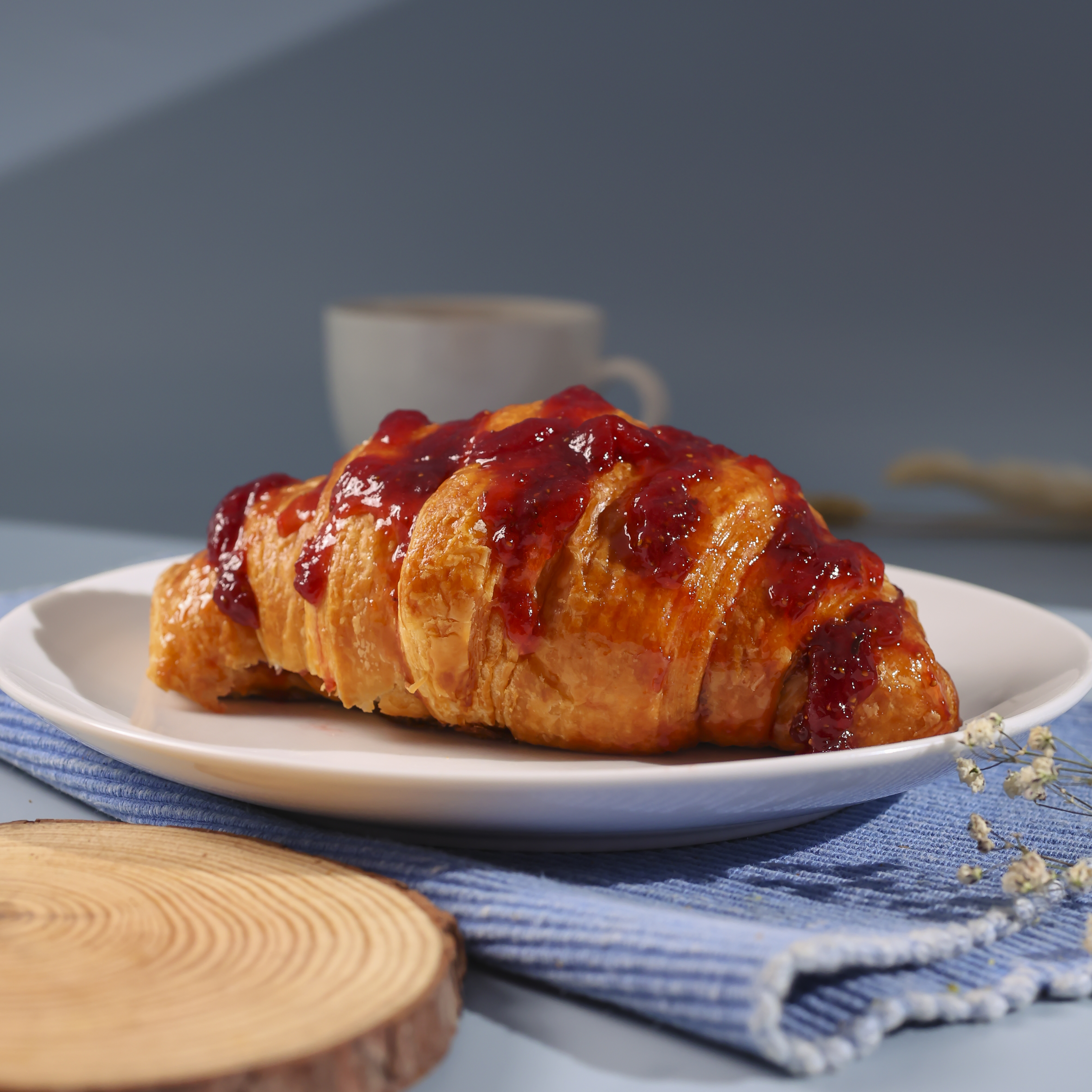 Flaky croissant topped with strawberry glaze served on a plate with coffee