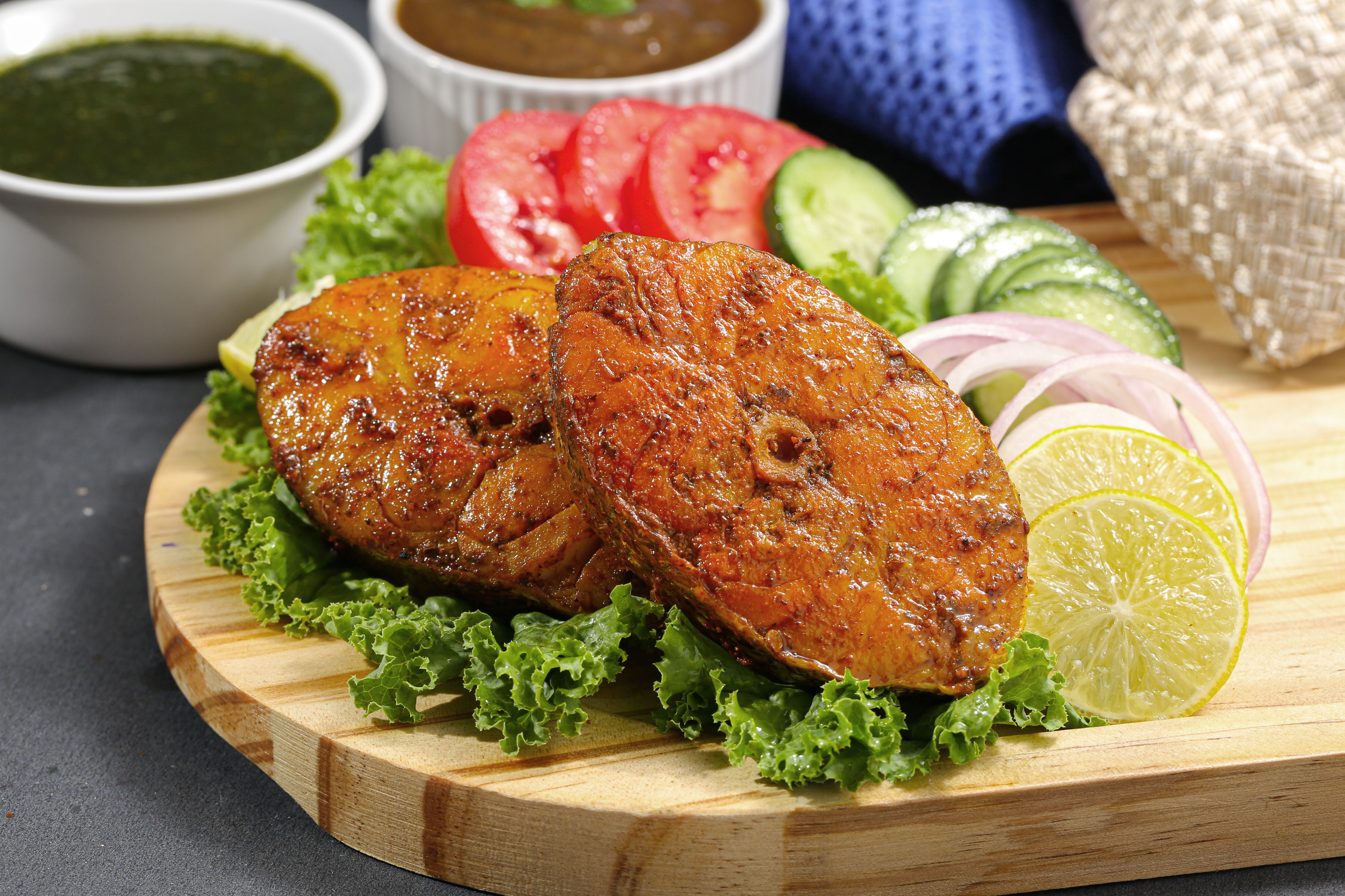 Spicy grilled fish fillets served with fresh salad and lemon slices on a wooden board