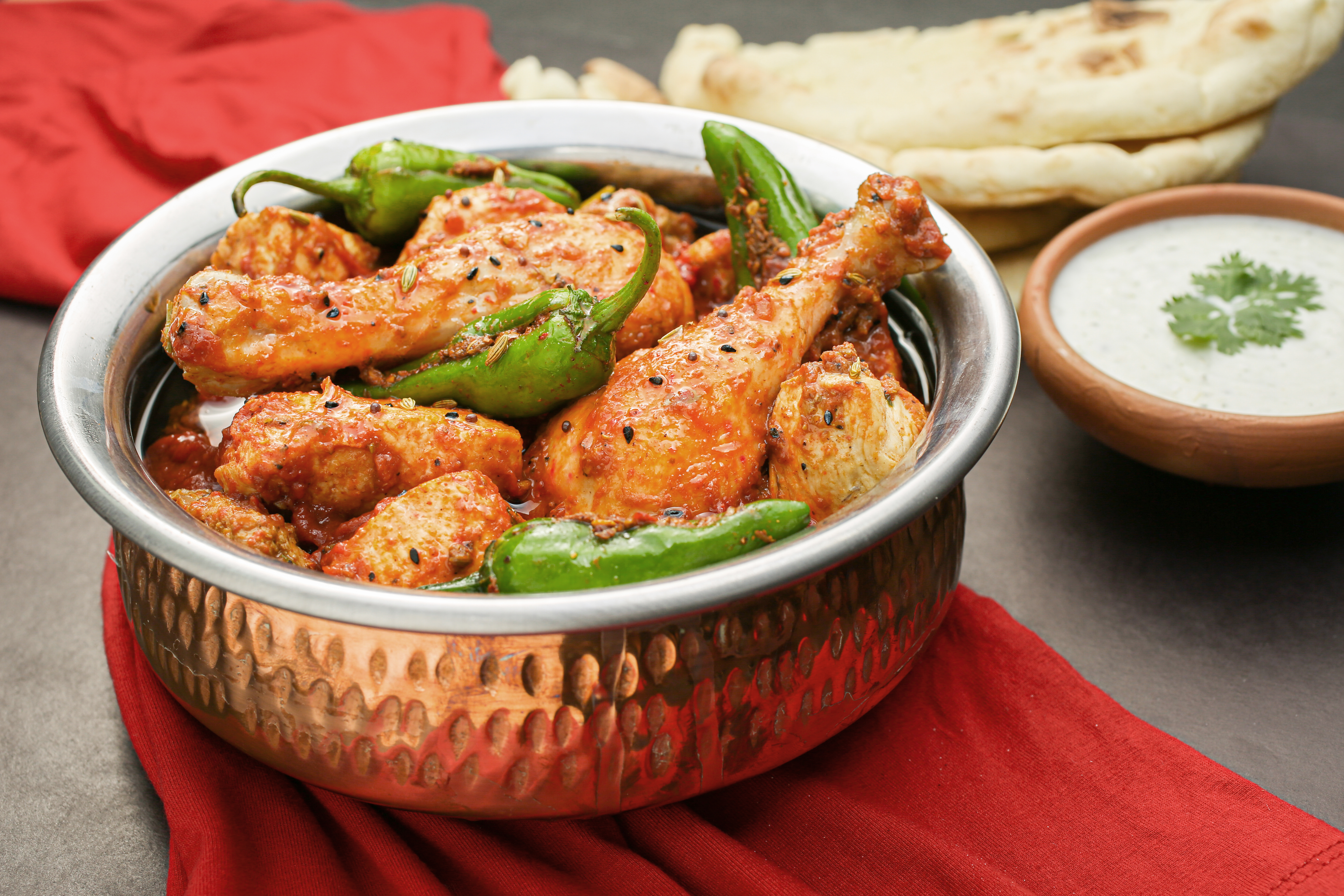 Spicy chicken curry with green chilies served in a traditional bowl with naan