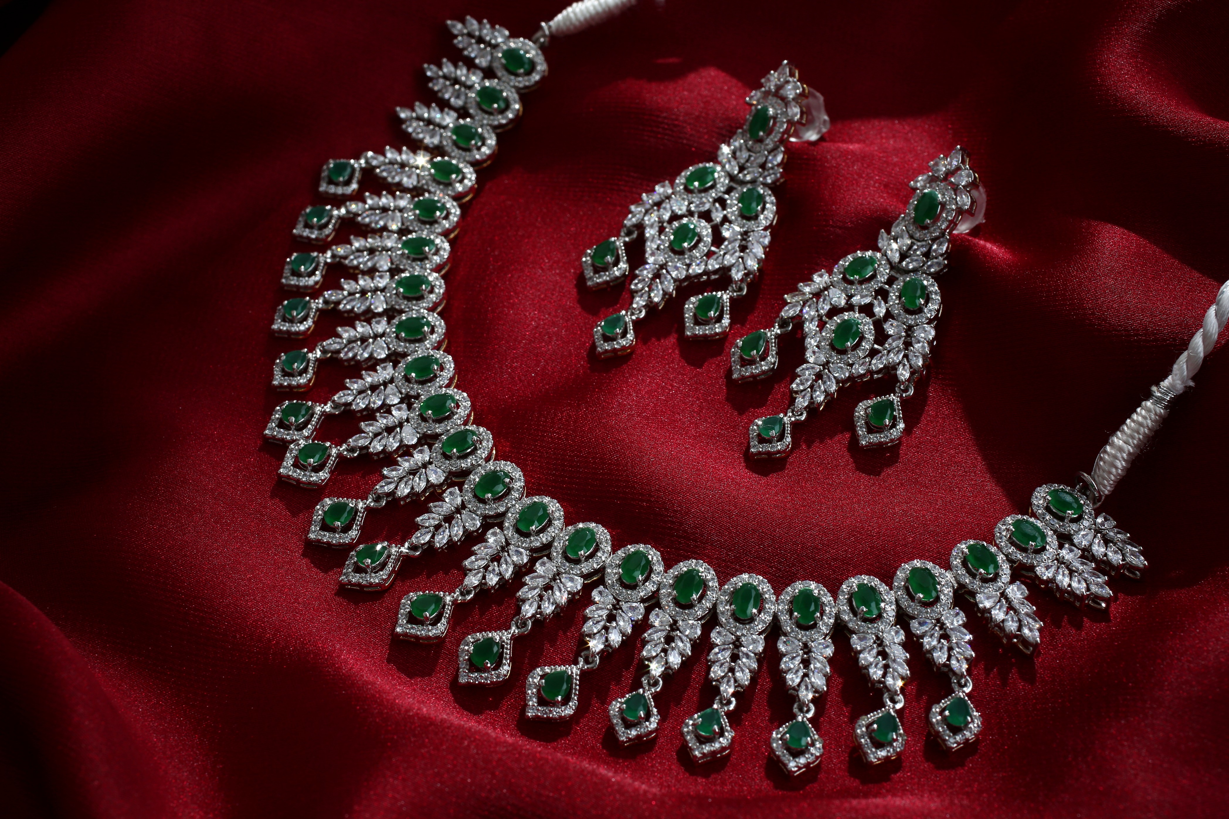 Luxury green gemstone necklace and earrings set on red fabric background